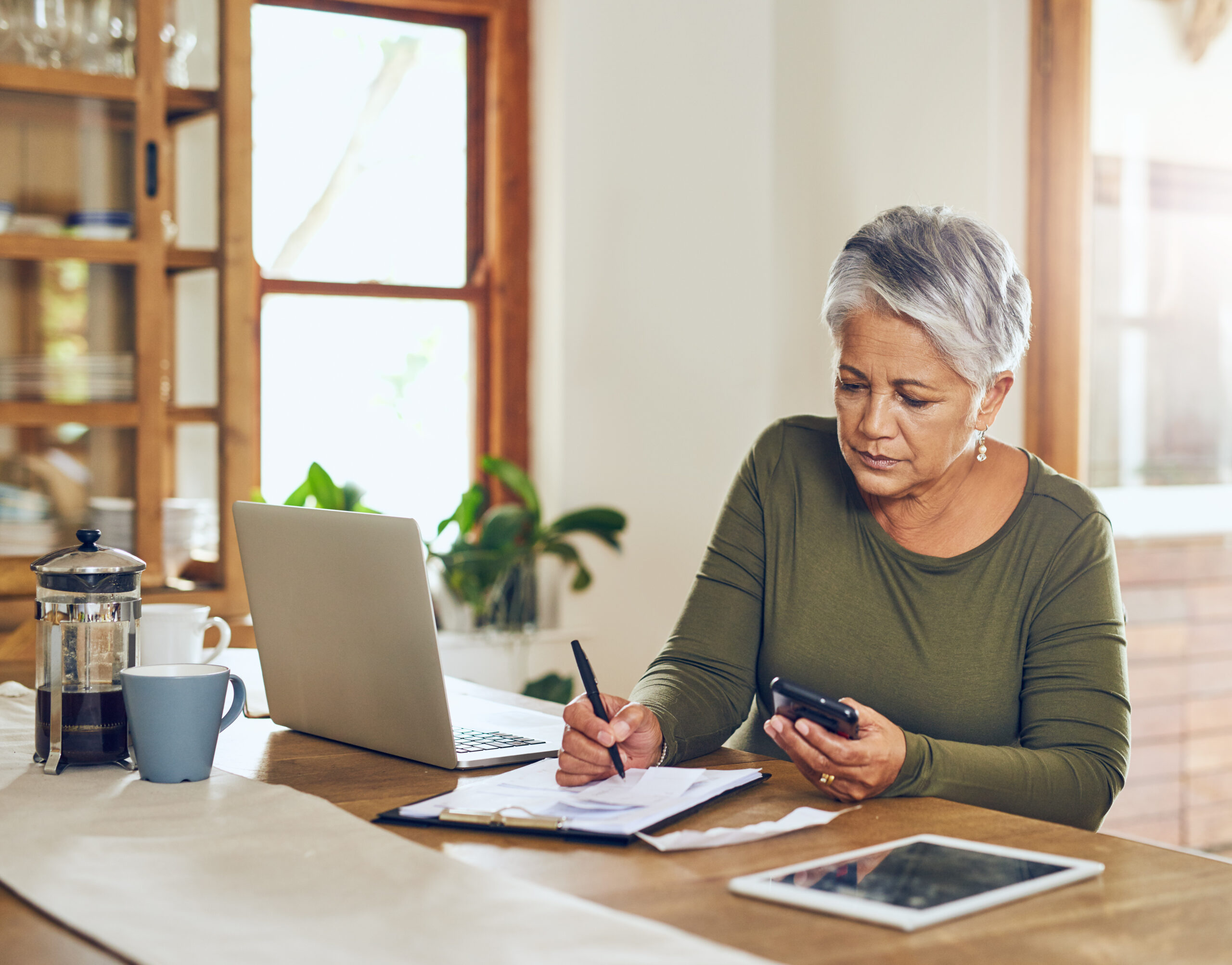 Woman sitting at kitchen table working on taxes with a laptop and smartphone