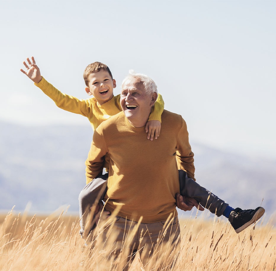 Grandfather gives grandson a piggy back ride in a field of wheat