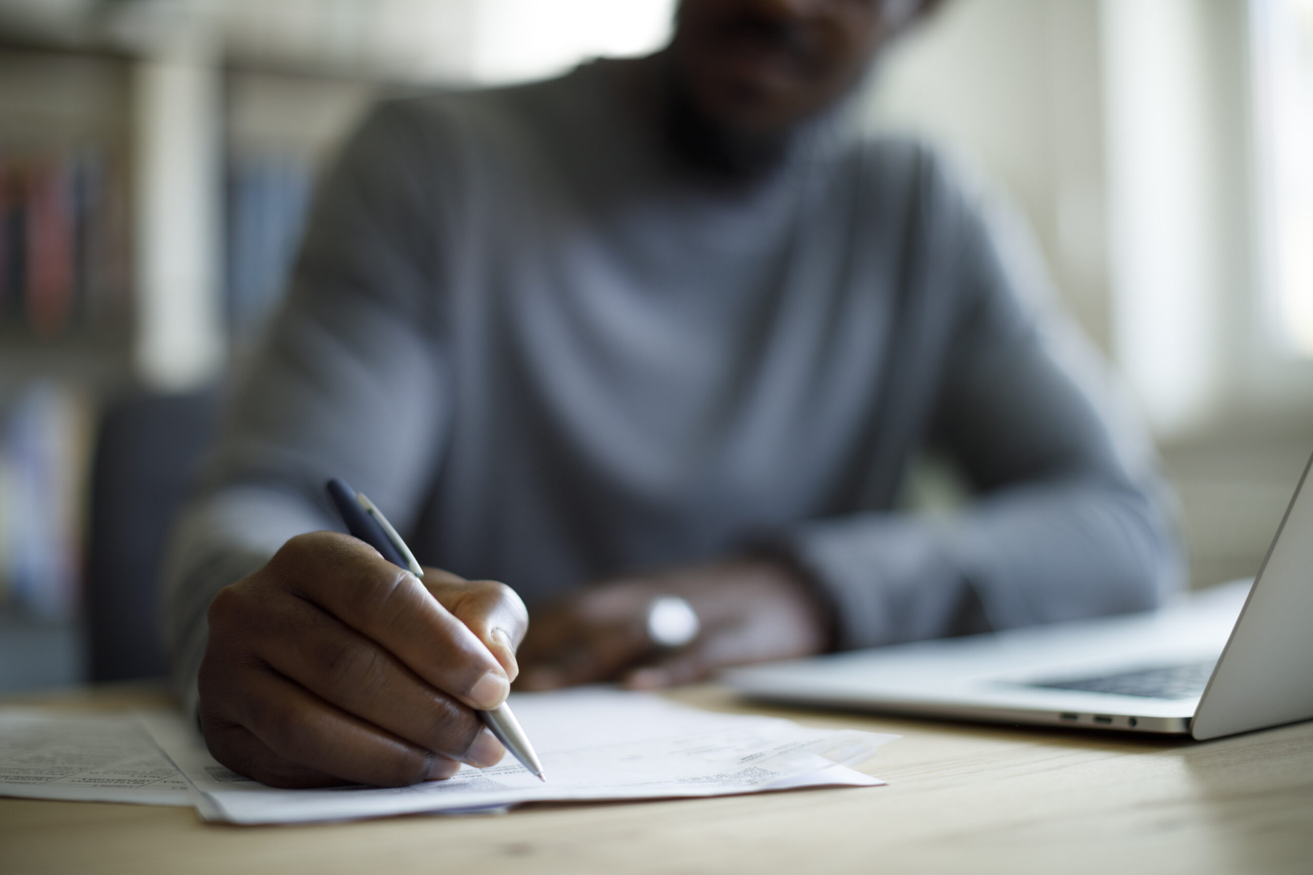 Person sitting at a laptop and holding a pen to paper