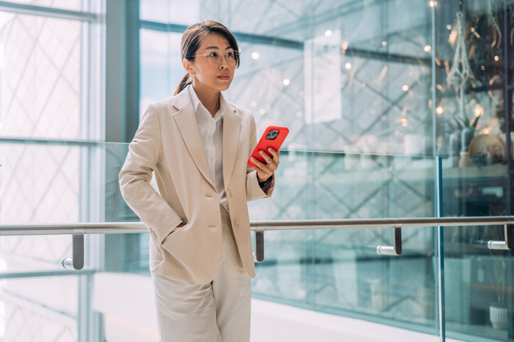 A woman using smartphone against modern office building in the city. Cybersecurity and finances.