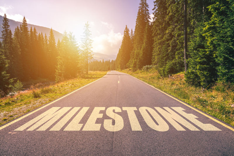 Two-lane road surrounded by trees, with the word MILESTONE written on it. A milestone for Carson Group.