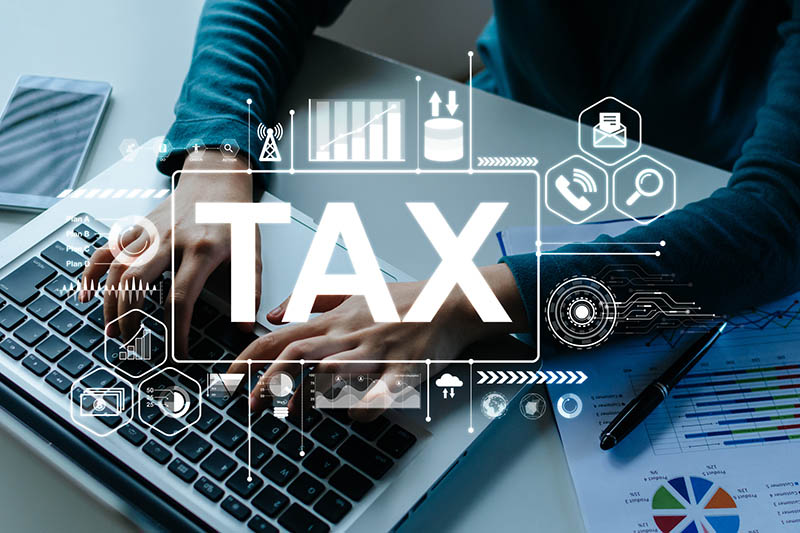 Hands using a laptop computer with a white TAX graphic icon overlayed on the image. Tax planning strategies.